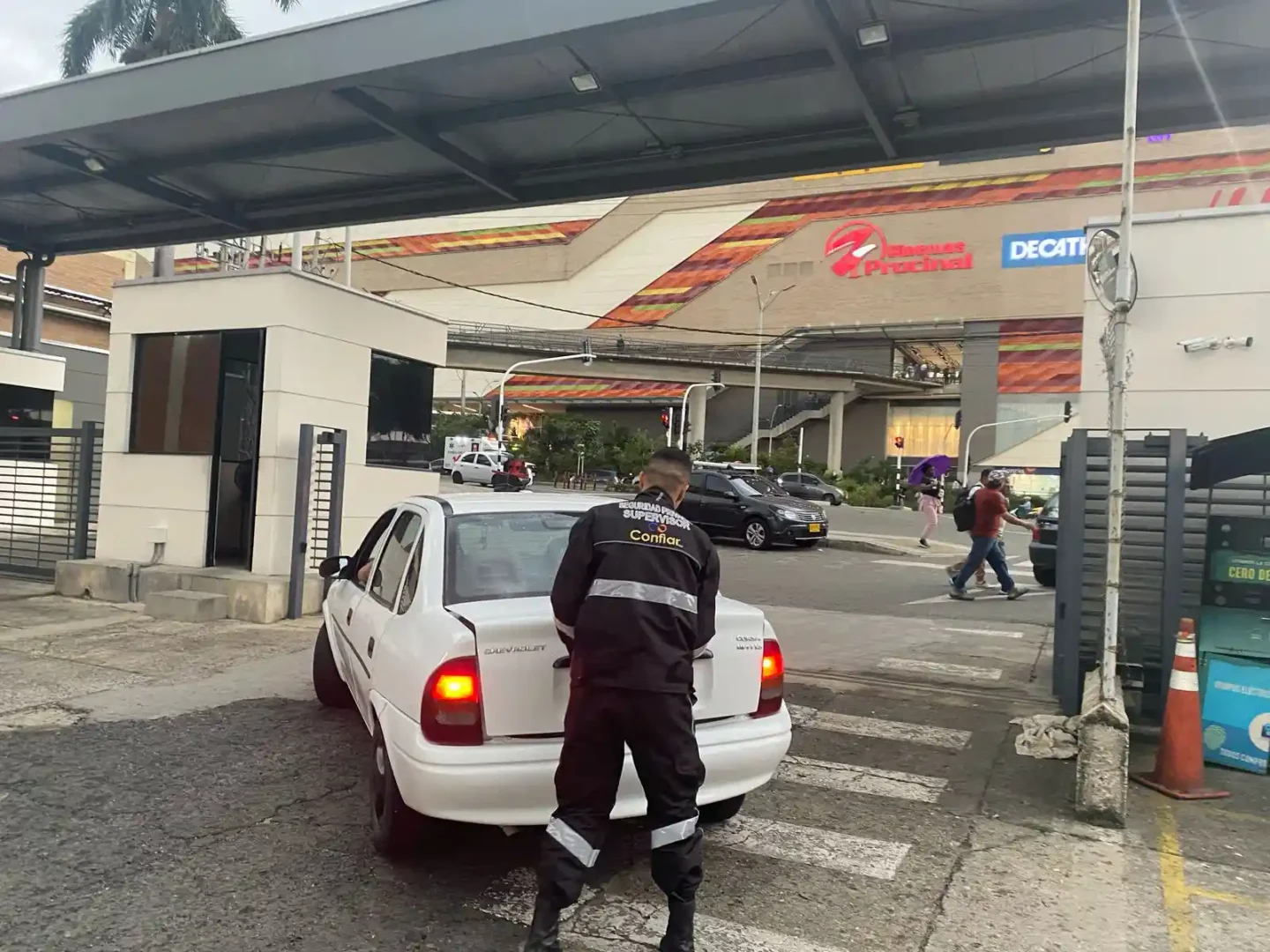 Guardia de seguridad inspeccionando baúl de vehículo en centro comercial.
